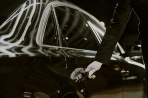 A chauffeur in a black suit and white gloves opening the door of a polished luxury black car, illustrating executive chauffeur services for corporate transportation florida.